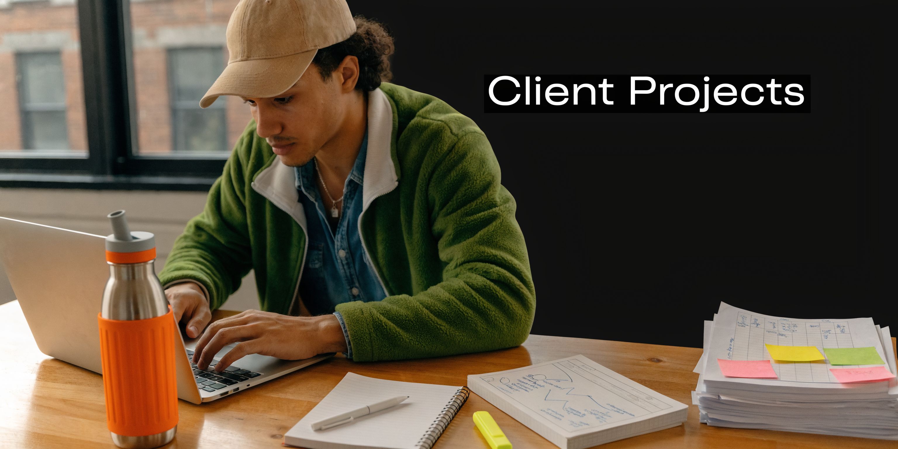 A young professional working on a laptop with documents and a water bottle on their desk.