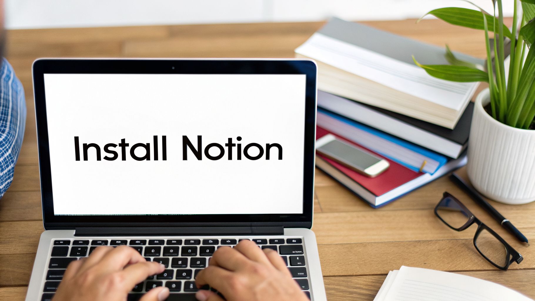 Person typing on a laptop showing 'Install Notion' on screen in a tidy workspace.