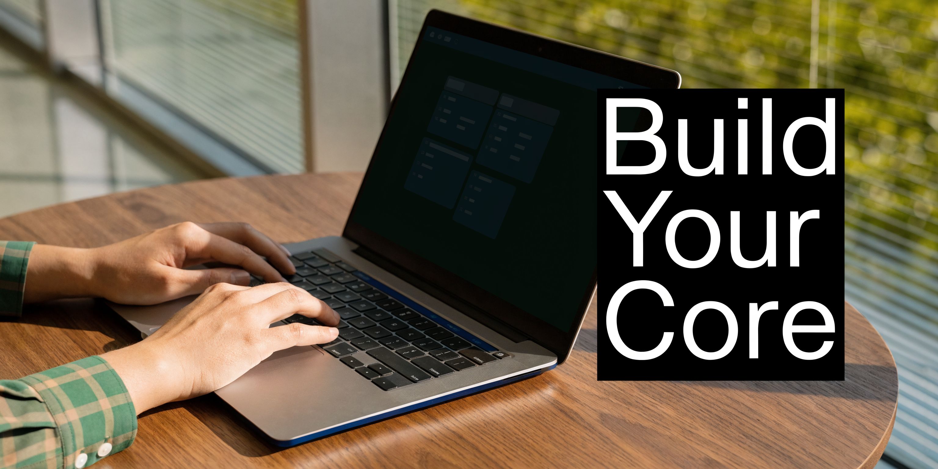 A person using a laptop on a wooden desk with the text Build Your Core displayed nearby.